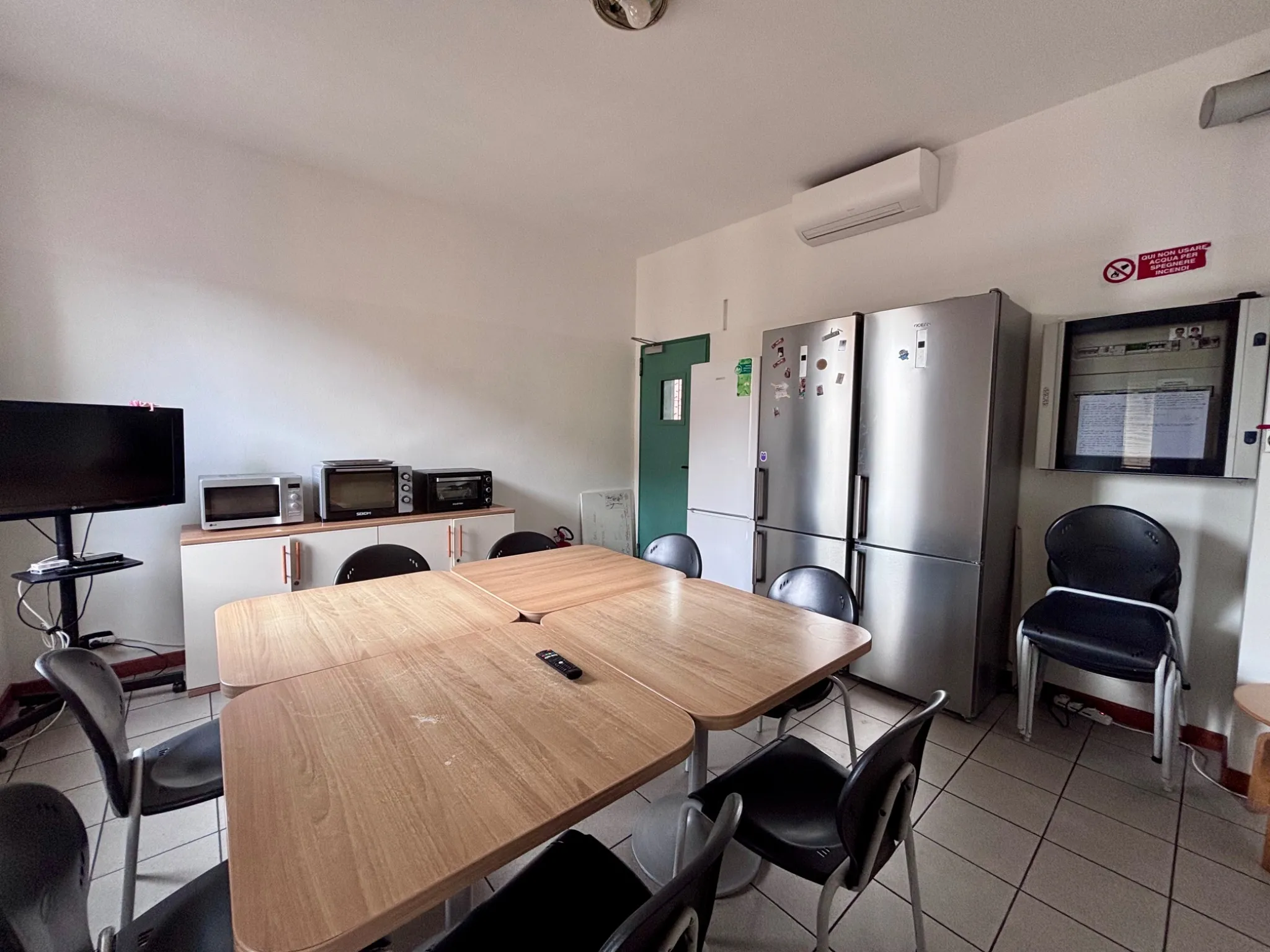 Cucina studenti attrezzata con tavolo, frigoriferi, microonde e televisore