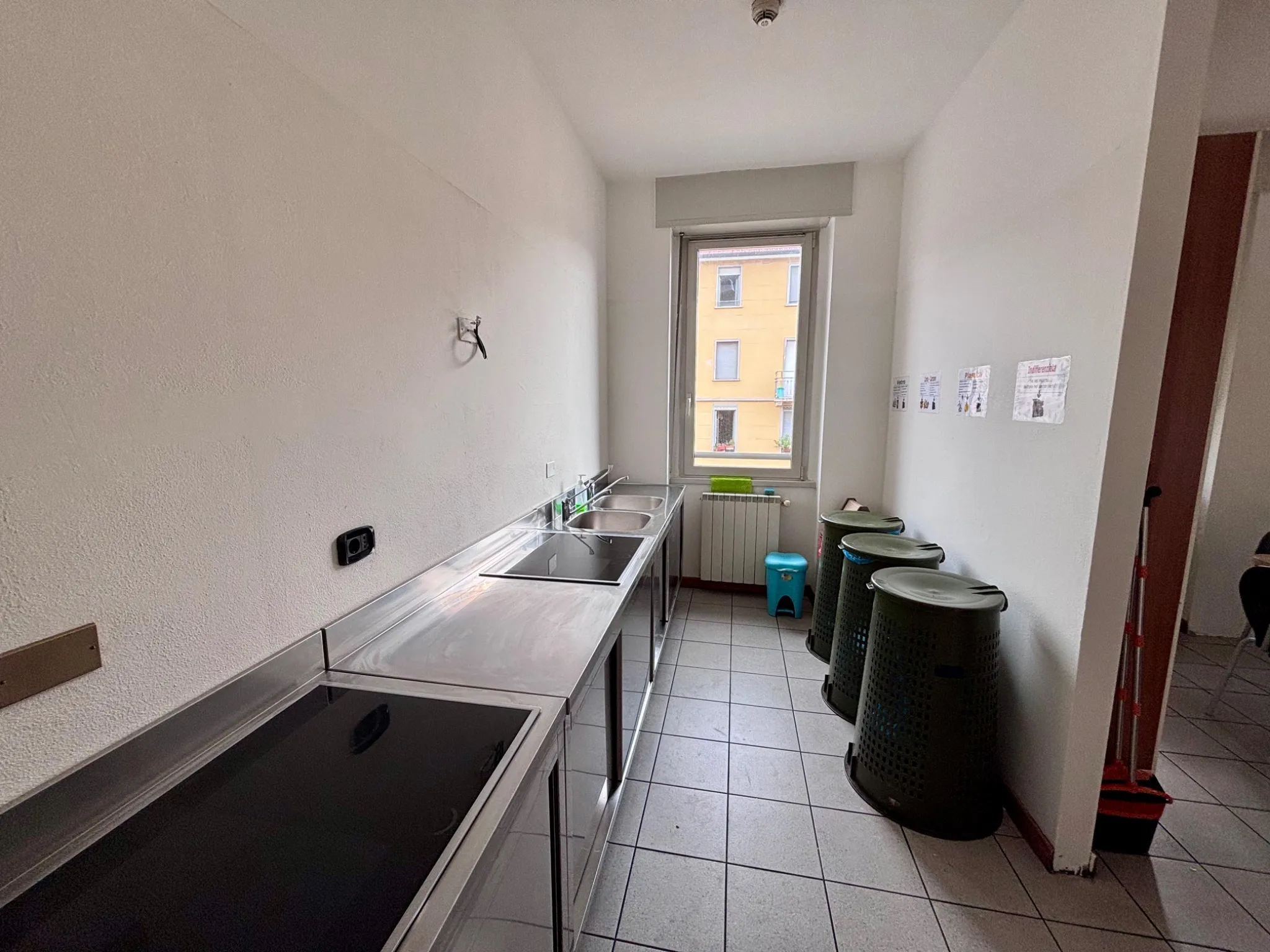 Area cottura della cucina studenti con piani a induzione e cestini raccolta differenziata