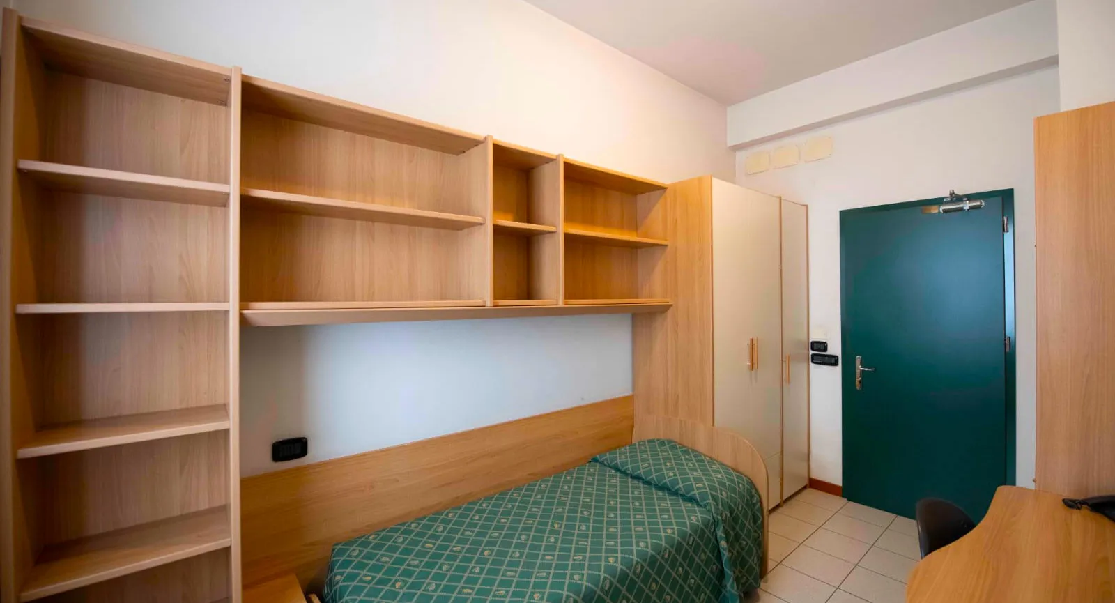 Stanza arredata con armadio, libreria con mensole e letto singolo al Pensionato Bertoni